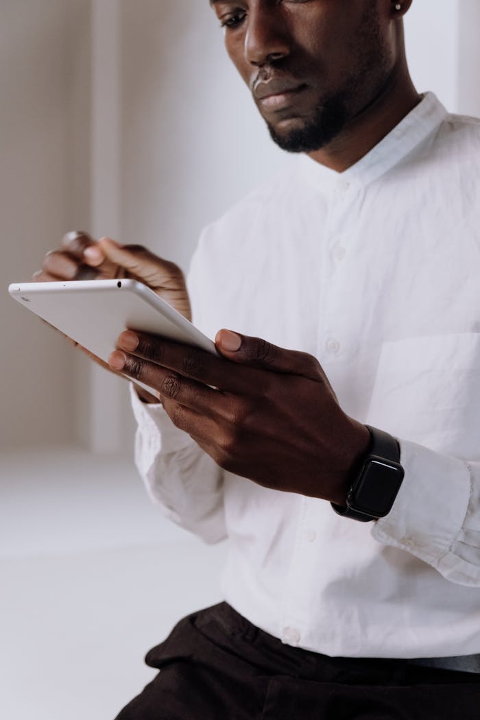 A focused man in a white shirt uses a tablet indoors, showcasing modern office technology.